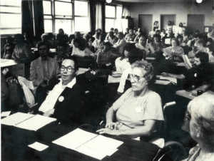 Photo en noir et blanc de l'assemblée générale de juin 1983 sur laquelle on voit une vingtaine de personnes assises, attentives